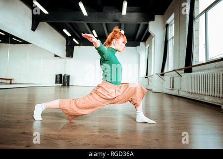 Beautiful slim yoga coach in a green turtleneck doing balancing asana Stock Photo