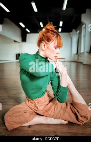 Young red-haired yoga instructor with hair bun feeling concentrated Stock Photo