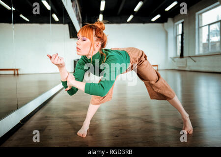 Red-haired professional yoga instructor in a green turtleneck standing in asana Stock Photo