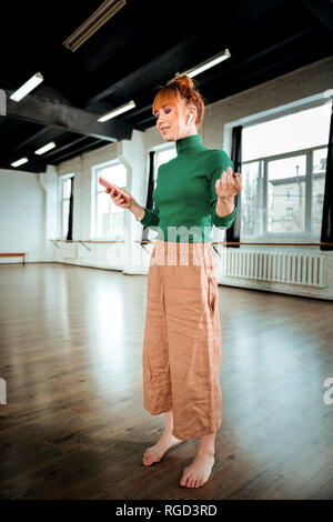 Red-haired professional yoga instructor in a green turtleneck reading a message Stock Photo