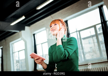 Red-haired professional yoga instructor in a green turtleneck speaking on the phone Stock Photo