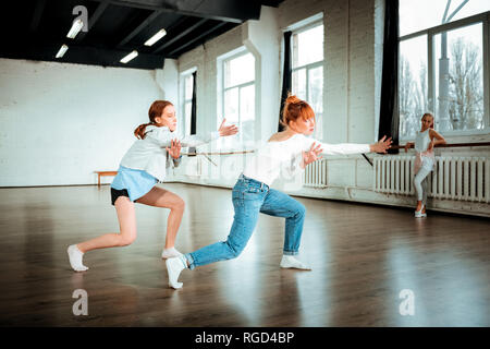 Beautiful red-haired professional dancer in blue jeans and her student dancing expressively Stock Photo
