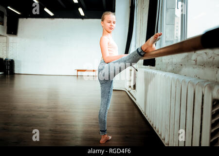 Beautiful blond teenager from generation z stretching her leg near the ballet bar Stock Photo