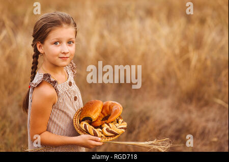 Girl with bread and buns in basket. Child is holding a lot of loaves in hands in the field. Stock Photo