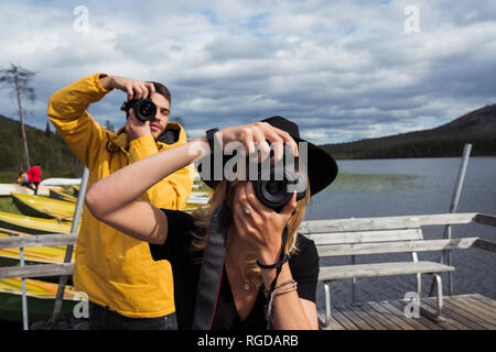 Finland, Lapland, man and woman taking pictures on jetty at a lake Stock Photo