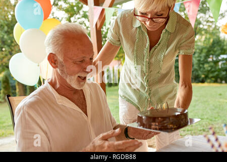 Woman handing over cake to happy husband on a garden party Stock Photo