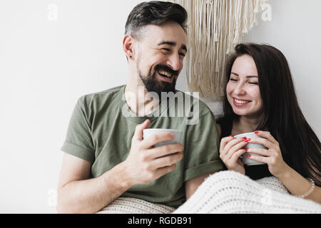 Happy couple sitting in bed, drinking coffee, having fun Stock Photo
