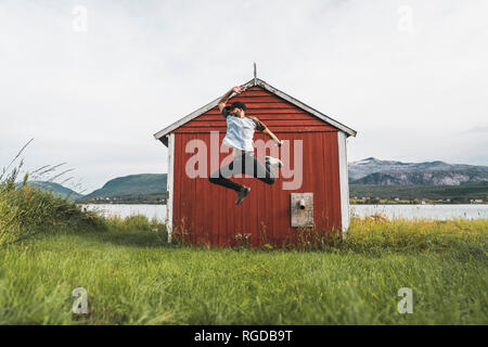 Young man jumping in front of red barn in Nothern Norway Stock Photo