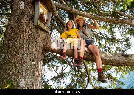 Portrait of smiling mother and daughter sitting in a tree Stock Photo