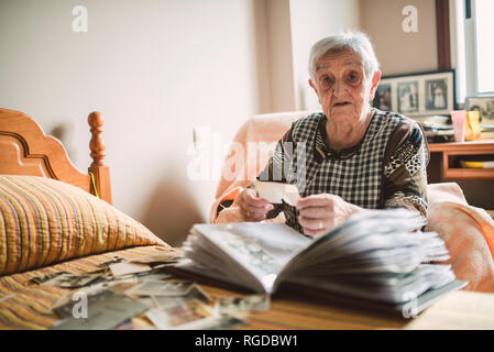 Portrait of senior woman adding old photos to a photo album at home Stock Photo