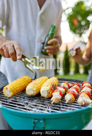 Corn cob and meat skewer on grill at barbecue in garden Stock Photo