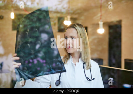 Female doctor looking at x-ray image behind windowpane Stock Photo