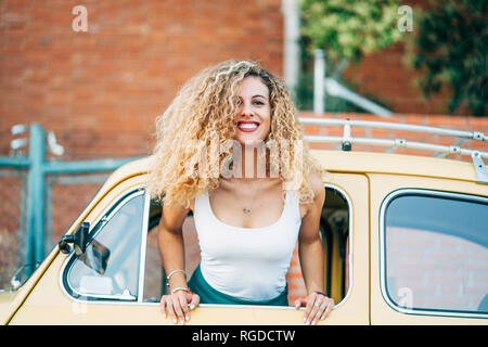 Portrait of happy blond woman leaning out of window of classic car Stock Photo