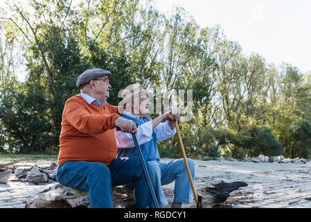 Two old friends sitting on a tree trunk by the riverside, sharing memories Stock Photo