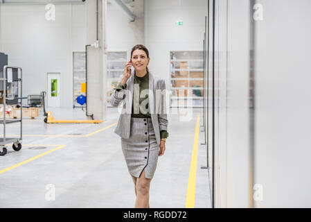 Businesswoman walking in factory workshop, talking on the phone Stock Photo