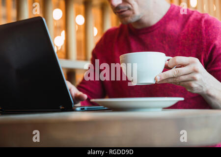Businessman sitting in a restaurant using laptop, drinking coffee Stock Photo