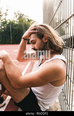 Young man sitting on basketball ground, tired and disappointed Stock Photo