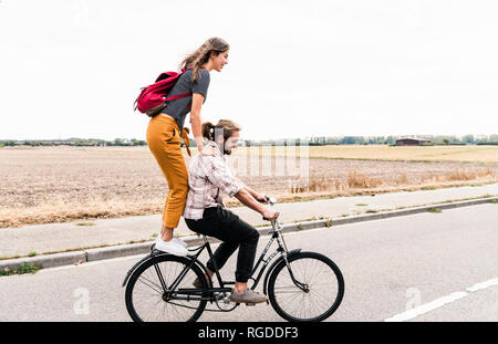 Happy young couple riding together on one bicycle on country road Stock Photo