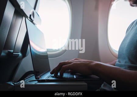 Man using laptop in airplane Stock Photo