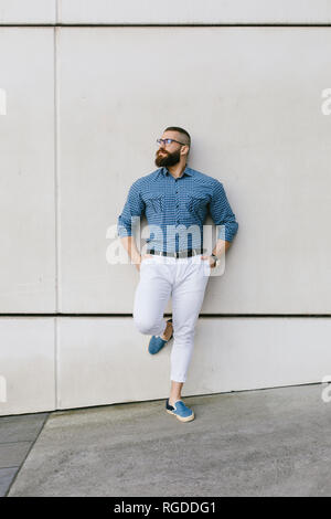 Bearded hipster businessman wearing glasses and plaid shirt leaning against wall Stock Photo