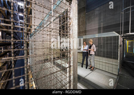 Women using laptop in high rack warehouse Stock Photo