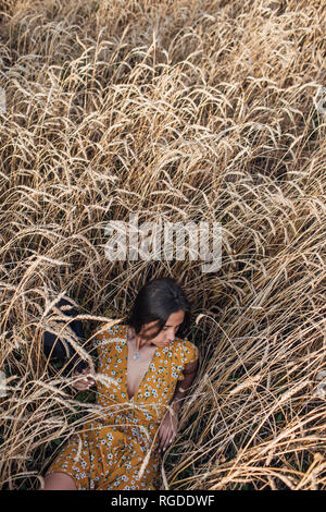 Young woman wearing summer dress with floral design lying in corn field Stock Photo