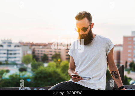 Cool bearded young man wearing sunglasses checking cell phone Stock Photo