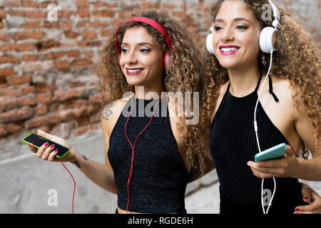 Portrait of happy twin sisters listening music with headphones and cell phones Stock Photo