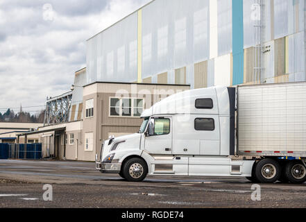 White big rig long haul semi truck with high cab and reefer semi trailer standing on parking lot waiting for loading and possibility of continuing to  Stock Photo