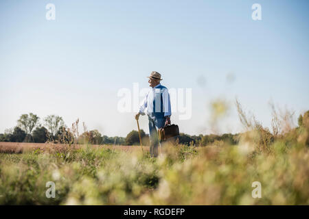 Senior man carrying traveling bag, walking in the fields Stock Photo