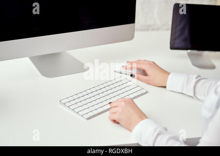Closeup of blurred female hands typing on white keyboard who is working at office and using modern computer Stock Photo