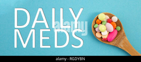 Daily meds text as treatment concept with wooden spoon full of colourful medicine on blue background Stock Photo
