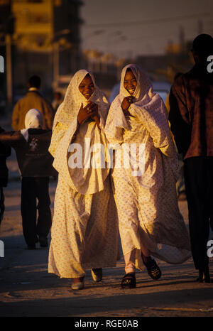 BORDJ EL HAOUAS, ALGERIA - JANUARY 16, 2002: two unknown women at sunset walking on the sidewalk Stock Photo