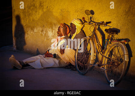 BORDJ EL HAOUAS, ALGERIA - JANUARY 16, 2002: two unknown men at sunset sitting with their bicycle Stock Photo