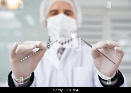 View from below of professional dentist looking at patient during diagnosis of teeth. Dentist holding restoration instruments. Doctor wearing white gloves, medical mask and cap. Stock Photo