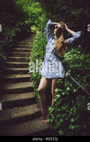 beautiful young girl in a blue dress posing on stairs outdoors wearing sunglasses, short dress, legs showing Stock Photo