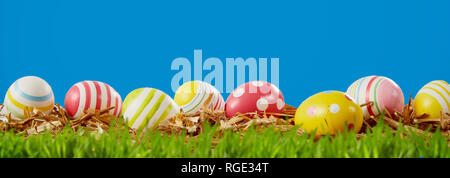 Happy Easter panorama banner with colorful decorative eggs nestling on the green grass in a meadow under a sunny blue sky with copy space for your hol Stock Photo
