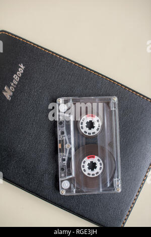 One plastic cassete for tape recorder and black notebook on a white background Stock Photo