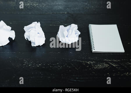 concept of drafting documents and struggling to write a text, set of scrunched paper balls and empty notepad on dark moody background Stock Photo