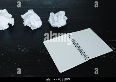 concept of drafting documents and struggling to write a text, set of scrunched paper balls and empty notepad on dark moody background Stock Photo