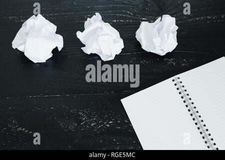 concept of drafting documents and struggling to write a text, set of scrunched paper balls and empty notepad on dark moody background Stock Photo