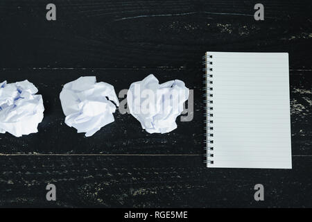 concept of drafting documents and struggling to write a text, set of scrunched paper balls and empty notepad on dark moody background Stock Photo