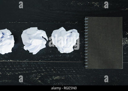 concept of drafting documents and struggling to write a text, set of scrunched paper balls and empty notepad on dark moody background Stock Photo