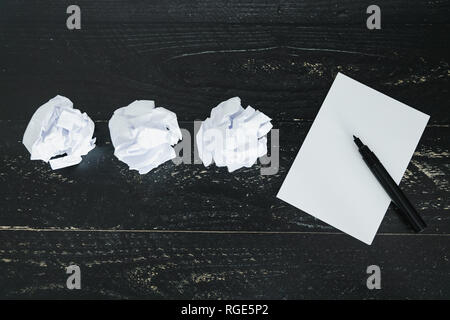 concept of drafting documents and struggling to write a text, set of scrunched paper balls and empty notepad on dark moody background Stock Photo