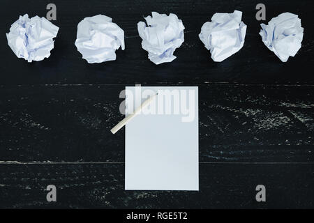 concept of drafting documents and struggling to write a text, set of scrunched paper balls and empty notepad on dark moody background Stock Photo