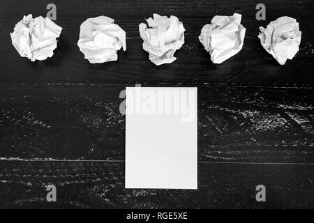 concept of drafting documents and struggling to write a text, set of scrunched paper balls and empty notepad on dark moody background Stock Photo