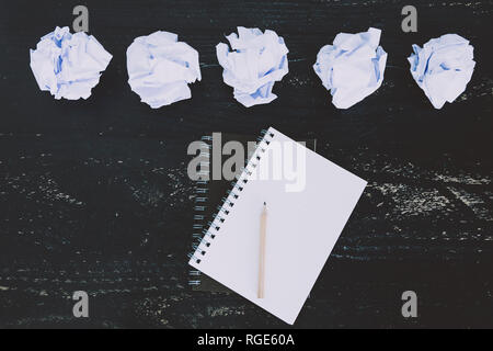 concept of drafting documents and struggling to write a text, set of scrunched paper balls and empty notepad on dark moody background Stock Photo