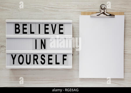 Lightbox with text 'Believe in yourself', clipboard with sheet of paper on a white wooden background, top view. From above, flat lay, overhead. Stock Photo