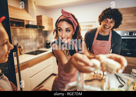 Happy parents and their daughter are preparing healthy meal together in the kitchen. Mother is putting banana slices in the blender. Stock Photo