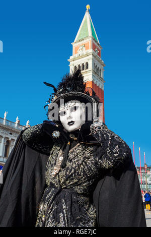 Vertical oriented portrait of an unidentified woman weared in vintage black costume, gloves, hat and white mask on San Marco square in Venice. Stock Photo